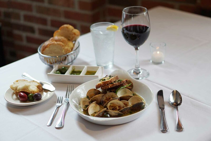 Clams with plated bread with olives. Dish of olive oil, side of bread with glass of water and wine